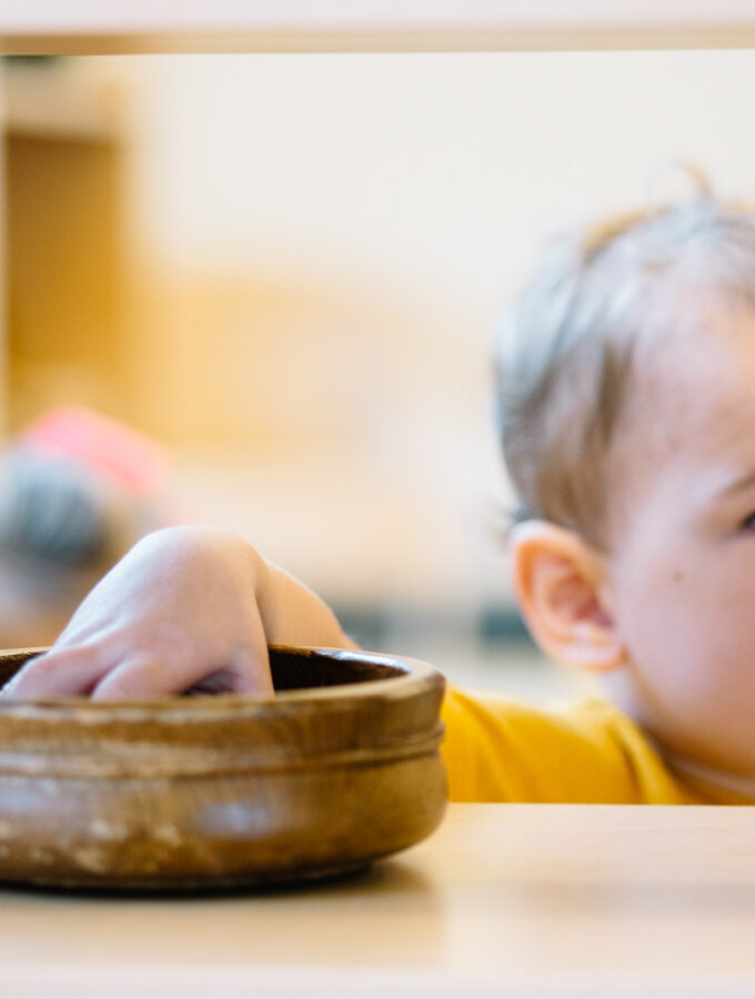 Montessori toddler taking a work from the shelf in the classroom