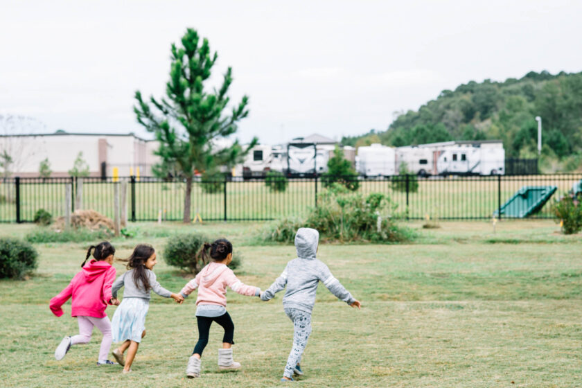 Four kids holding hands and running outside.